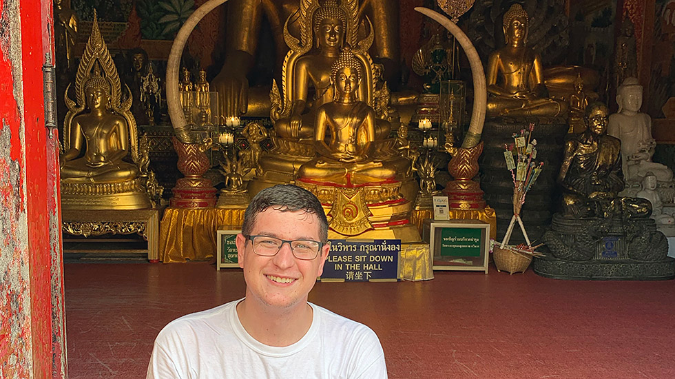 Caleb Moon in front of buddha statues.