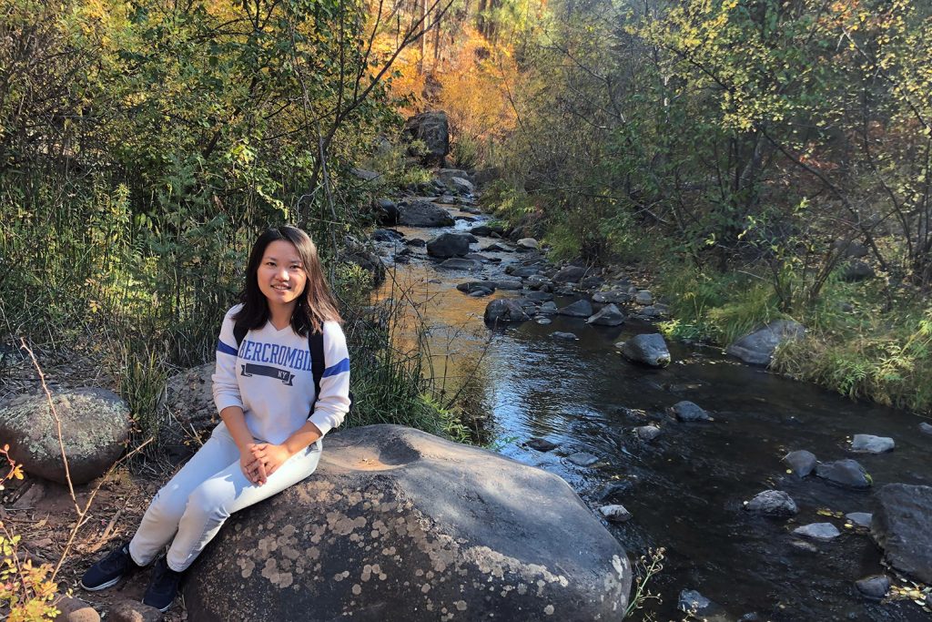 Naijia Hao sits on a large rock beside a stream in New Mexico.