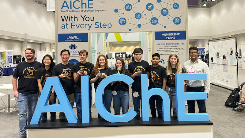 Group of CBE students in front of a large AIChE sign.